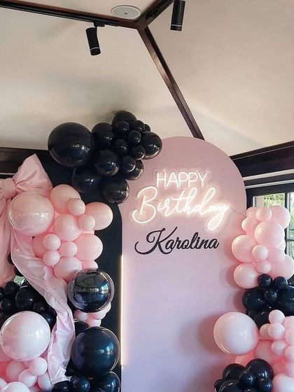 A stylish pink and black theme for a house party, featuring a custom arched backdrop with a neon sign and a beautiful balloon garland.