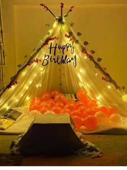 A cozy teepee tent setup for a birthday. The tent is decorated with fairy lights and filled with orange balloons, creating a perfect spot for a private celebration.