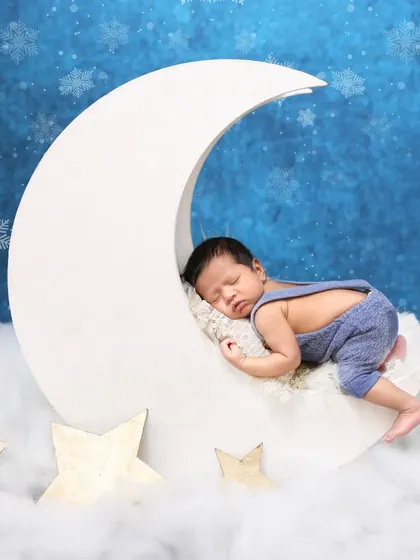 For a touch of magic, I love creating dreamy scenes like this one. Here, a peacefully sleeping baby rests on a crescent moon prop, surrounded by soft clouds and stars. Your baby's safety is always my priority during these creative newborn poses.