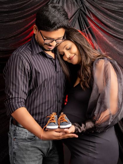 A sweet announcement photo. The couple holds a pair of tiny baby shoes, their heads together in a tender pose that signifies their journey into parenthood.