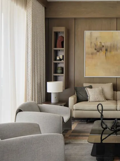 The living room at 'Pad by the Bay' is a composition of textures. The warmth of the oak-paneled wall is balanced by the soft gray of the armchairs and the abstract sculpture on the coffee table, creating a sophisticated and curated living space.