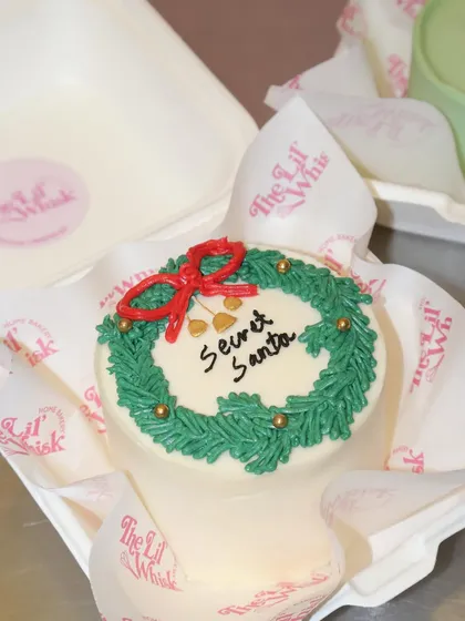 A "Secret Santa" bento cake, featuring a festive wreath and a red bow. The perfect sweet surprise for your holiday gift exchange.