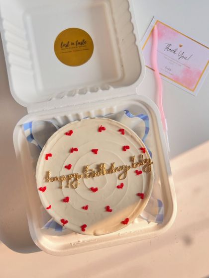 A simple and elegant birthday wish. This cake features "happy birthday izy" in beautiful gold script on a swirled white buttercream base, dotted with tiny red hearts.
