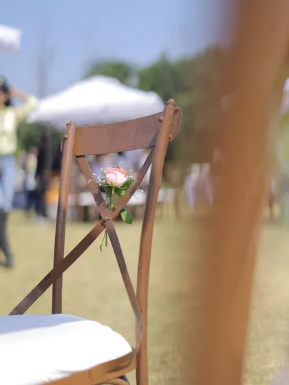 Even the chairs get a touch of magic. A simple yet elegant detail with a single pink rose and baby's breath tied to the back of a cross-back chair at an outdoor carnival event.