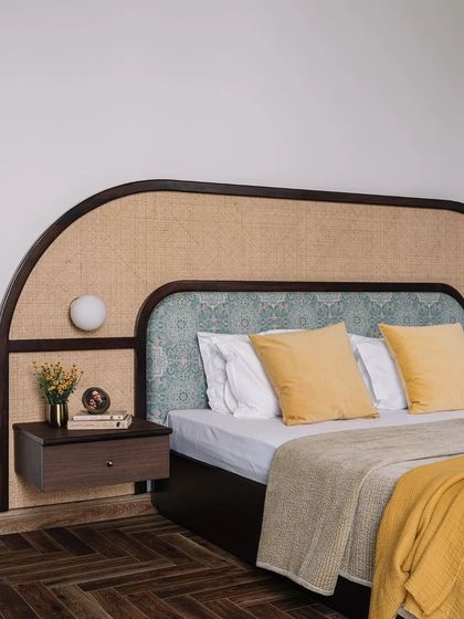 This bedroom features a beautiful custom headboard that combines a curved wooden frame with cane weaving and a patterned fabric inlay.