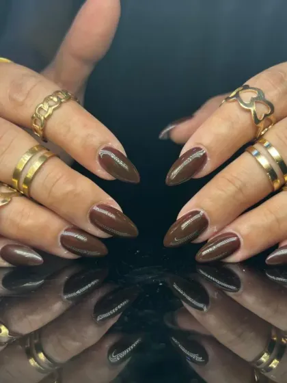 A full view of the chic dark brown manicure, styled with gold rings.