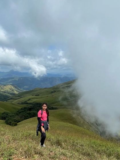 A trekker stands at the edge of the trail as a massive cloud rolls over the Nethravathi peak, showcasing the dramatic weather.