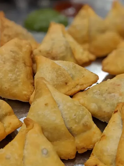 A tray of classic, triangle-shaped Punjabi Samosas, fried to a perfect golden brown.
