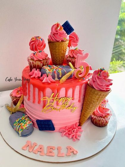 An overloaded drip cake with ice cream cones and cupcakes, making it a dream come true for any sweet tooth.