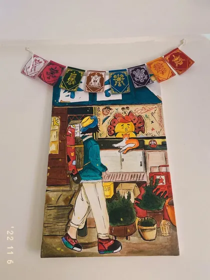 A finished illustrative painting hanging on the wall. This piece has a Japanese-inspired street scene aesthetic, complete with colorful prayer flags.