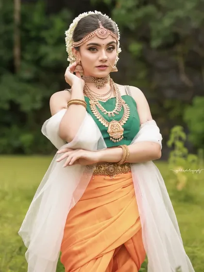 A graceful pose from the Sakhi series, this portrait showcases the full outfit with its vibrant orange and green colors.