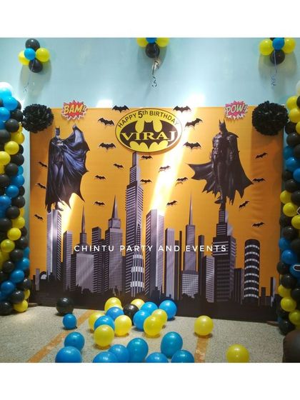 A Batman themed 5th birthday party with a Gotham city skyline backdrop. The decoration uses black, yellow, and blue balloons and character cutouts to create a superhero atmosphere.