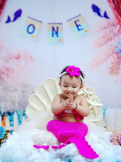 Our little mermaid claps her hands with glee, sitting in a large white seashell. This is a perfect theme for a first birthday.