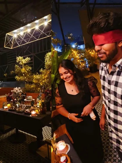 The moment of reveal. A blindfolded man is led by his partner to a beautifully decorated table, his smile showing he knows something special is about to happen.
