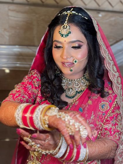 A candid moment of a bride in a pink lehenga, looking at her kalire. Her makeup is soft and pretty, with a focus on rosy cheeks and shimmery eyes.