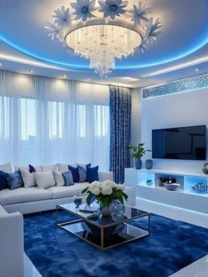 We used dramatic lighting to create a unique ambiance in this living space. The coffered ceiling features bold blue cove lighting, which contrasts with the intricate floral chandelier, while the back-lit TV console adds another layer of soft, ambient light.