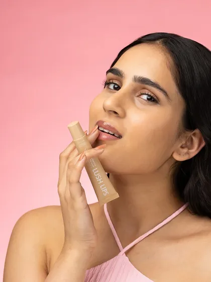 A close up lifestyle shot focusing on the application of a nude lip gloss. The model's relaxed expression and the soft lighting create a natural, effortless beauty look that is highly aspirable.