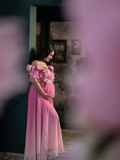 A quiet, artistic portrait of the mother-to-be, framed by a doorway and soft floral elements. This shot captures a moment of serene reflection amidst the celebration.