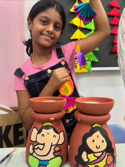 This student is thrilled with her finished Diwali crafts, including painted holders and a paper hanging.