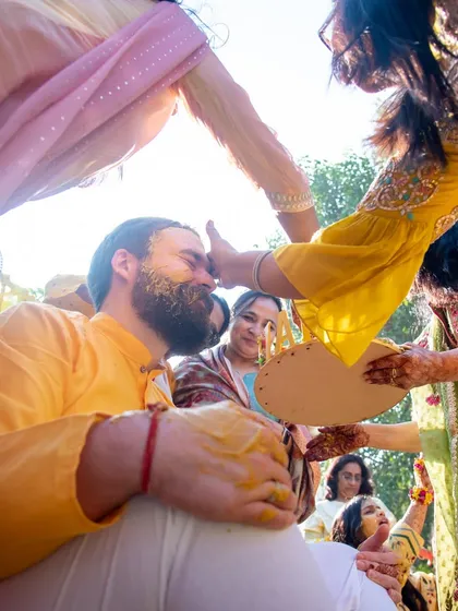 The haldi ritual in action. A low-angle shot capturing family members applying turmeric paste to the groom.