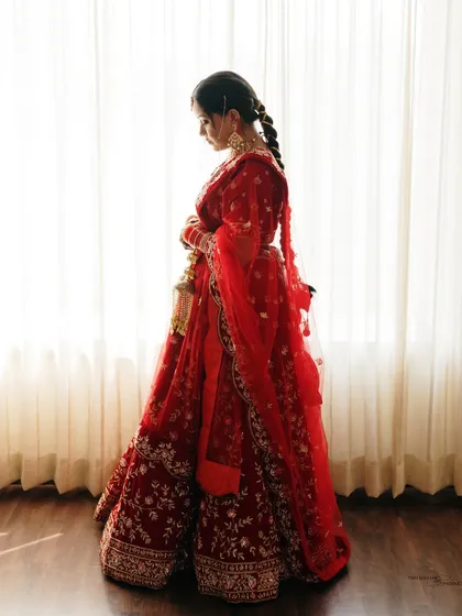 A silhouette of the bride against a brightly lit window. This artistic shot creates a sense of mystery and highlights the beautiful form of her red wedding lehenga.