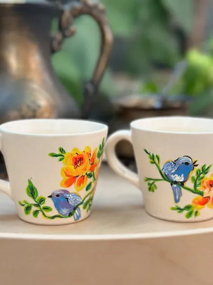 A lovely pair of ceramic mugs featuring little blue birds perched among yellow roses.