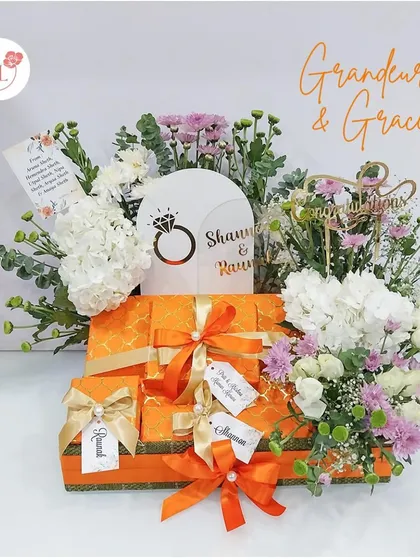 An engagement hamper that exudes grandeur and grace. The bright orange boxes are personalized with tags for the couple and complemented by fresh white and purple flowers.