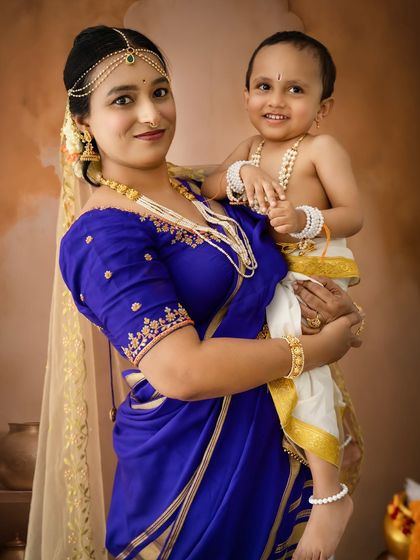 A mother in a striking blue saree holds her smiling son, dressed as Krishna. This portrait highlights the rich colors and textures of their traditional attire.