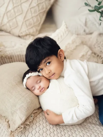 A protective and sweet moment as an older brother holds his sleeping newborn sister. The neutral tones and soft textures create a timeless feel.