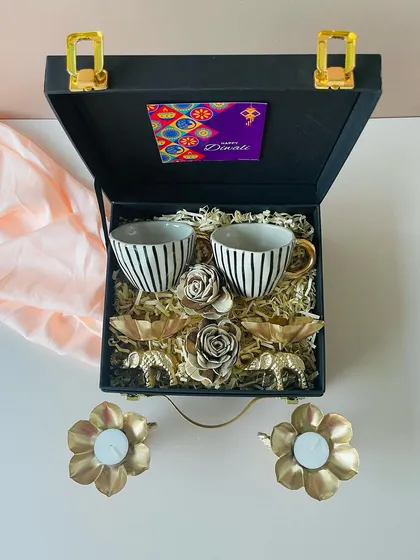 A closer look at this elegant hamper in a black suitcase box. It includes two striped ceramic cups with gold handles and ornate golden elephant T-light holders, offering luxury at a great price.