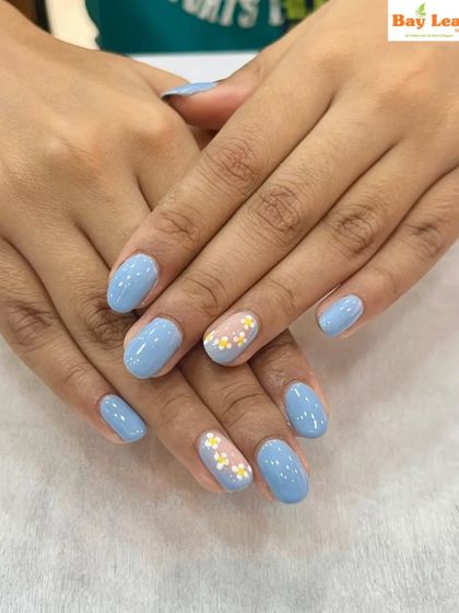 The perfect pastel look. These nails feature a lovely soft blue gel polish with two accent nails adorned with delicate, tiny yellow and white floral art.