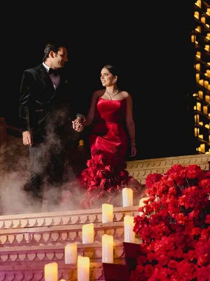 The couple makes a grand entrance down steps lined with red roses and candles, with smoke effects adding to the drama and romance of the moment.