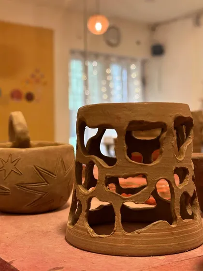 A hand-carved terracotta lantern, glowing warmly from within. This piece was made by a student exploring piercing techniques.