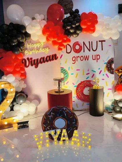 A sweet 'Donut Grow Up' theme for a second birthday. The decor includes a donut-print backdrop, donut-shaped props, and a marquee number '2', all in a fun red, black, and white color scheme.