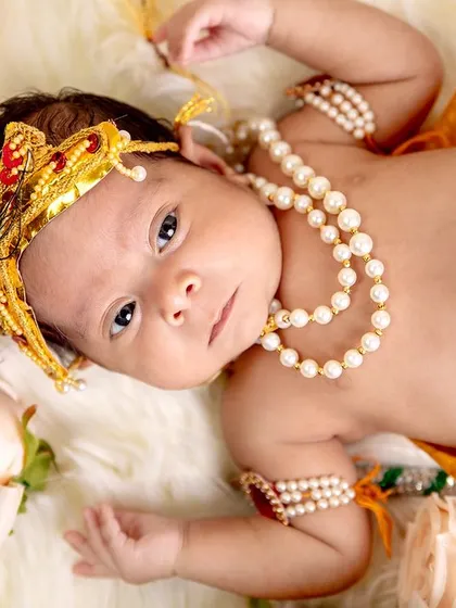 A close-up portrait of a newborn Krishna, showing the intricate details of the costume, from the peacock feather crown to the pearl armlets. We focus on quality in every shot.