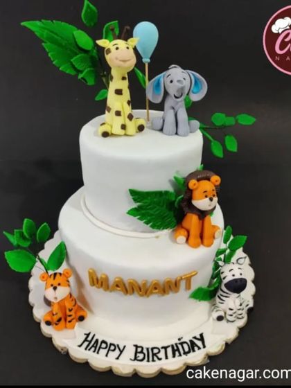 A clean and modern two-tiered jungle cake. This white cake is decorated with cute fondant animals like a giraffe, elephant, lion, and tiger, with green leaves for a pop of color.