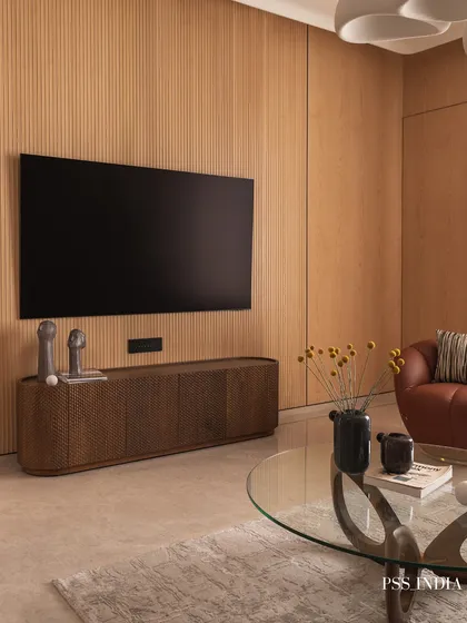 A different angle of the living room, showing the interplay between the fluted wood TV wall, the sculptural coffee table, and the pop of color from the reddish-brown armchair.