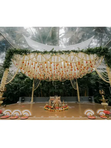 The full mandap setup inside a transparent tent, combining the grandeur of traditional floral decor with the beauty of the surrounding natural greenery.