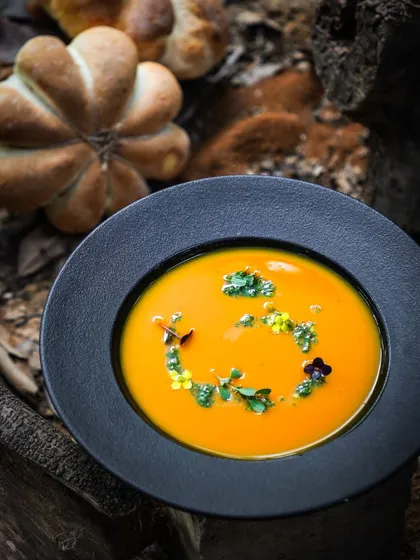 A beautiful bowl of pumpkin soup, garnished with edible flowers. This dish is part of our Thanksgiving celebration, a time to express gratitude to our guests and team.