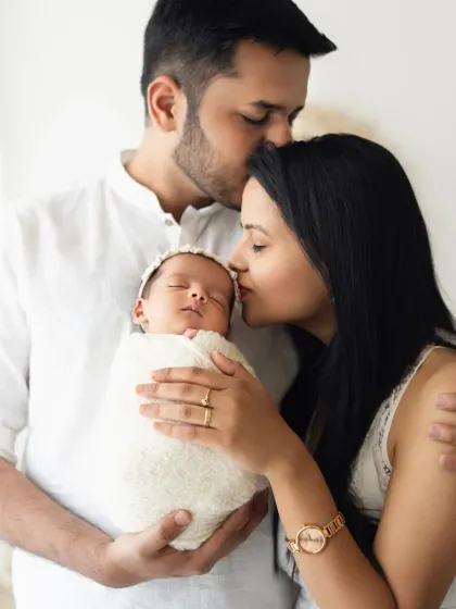 A new family of three shares a loving embrace, with the father's arm around the mother who is holding their sleeping newborn. A classic newborn with parents portrait.