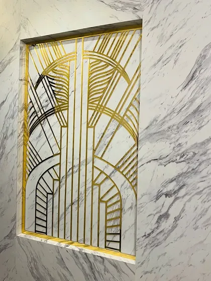 To make a memorable first impression, we created this Art Deco-inspired partition for an entryway. The custom-designed geometric pattern in gold and black metal set against a marble-finish wall adds a touch of timeless glamour.