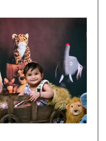 A big, happy smile from this little girl in her jungle-themed photoshoot. Sitting in a wooden cart with her animal friends, she is clearly enjoying her wild adventure.