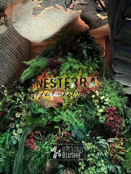 The Nesterra logo glowing warmly amidst the dense foliage of the custom installation, viewed from a different angle.