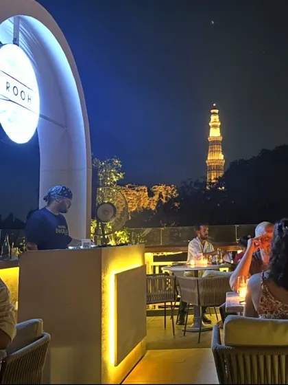 As dusk settles, the vibe on our rooftop shifts. Here, a DJ sets the mood for one of our sundowner events, blending soulful beats with the incredible view of a lit-up Qutub Minar.