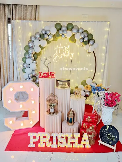 A sophisticated birthday setup with an olive green, white, and silver balloon arch. The large marquee number '9' and plinth arrangement complete the look.