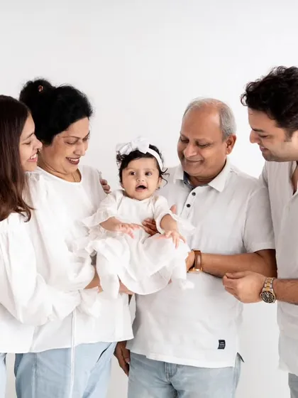 A timeless multigenerational family portrait, celebrating the connection between grandparents, parents, and their new baby. The coordinated white outfits and clean background create a classic, elegant look that will be cherished for years.