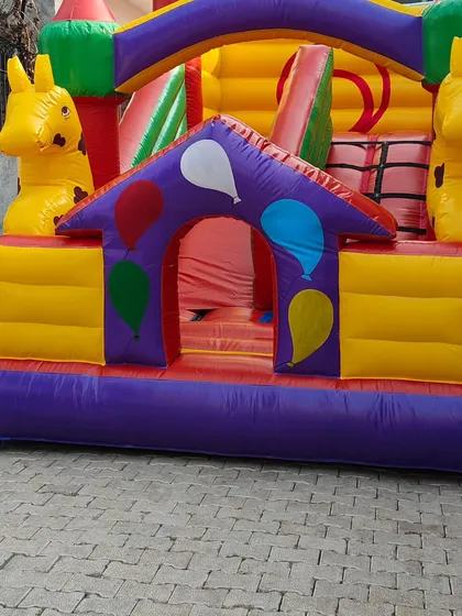A house-themed bouncy with giraffe figures. This design includes a small internal slide and a tunnel entrance.