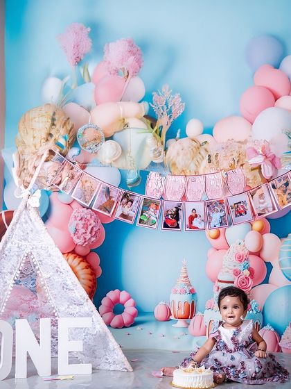 One year of magic, mischief, and a million memories. This wide shot captures the full splendor of the first birthday setup, with a photo banner showcasing the baby's journey through her first year.