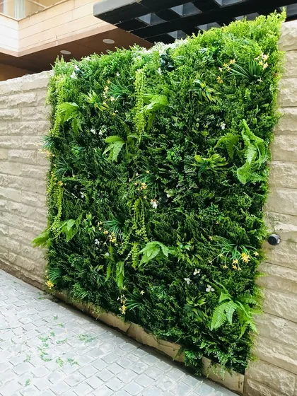 An outdoor vertical garden panel installed on a stone-clad boundary wall. The mix of ferns and delicate white flowers adds a touch of softness and greenery to the home's exterior.