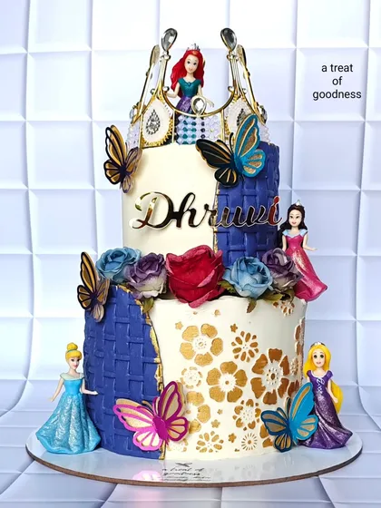 A magical two-tiered cake for a Disney princess celebration. This non-fondant creation brings together multiple stories with detailed character toppers, a golden crown, and a blend of buttercream textures like basketweave and gold stenciling.